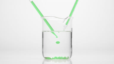 Dropper drips green oil in water in beaker which sink to bottom