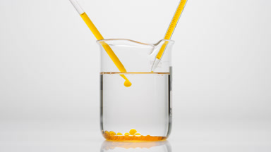 Dropper drips orange oil in water in beaker which sink to bottom