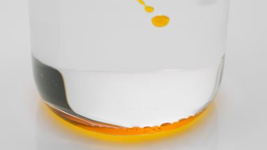 Orange transparent bubbles sink to bottom of beaker with water