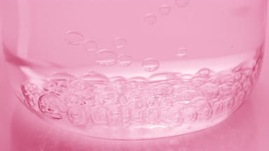 Bubbles sink to bottom of beaker with water on pink background