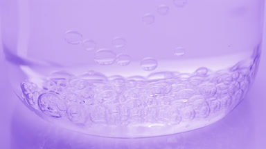 Bubbles sink to bottom of beaker with water on purple background