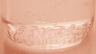 Bubbles sink to bottom of beaker with water on beige background