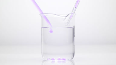 Dropper drips purple oil in water in beaker which sink to bottom