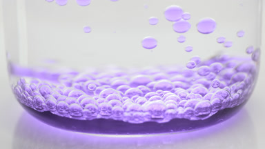 Purple transparent bubbles sink to bottom of beaker with water