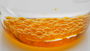 Orange transparent bubbles sink to bottom of beaker with water