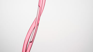 Rose oil is flowing down in connecting tubes on grey background