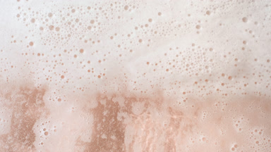 Macro of water wave flows creating foam on beige background