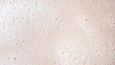 Macro shot of water with a lot of foam flows on beige background