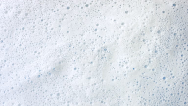 Macro shot of water with a lot of foam flows on blue background