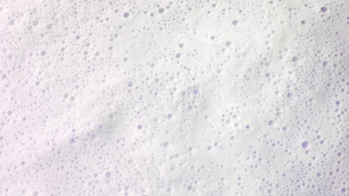 Macro shot of water with a lot of foam flows on violet background