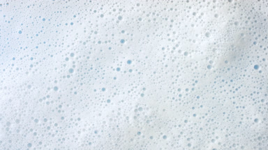 Macro of water with a lot of foam flows on pale blue background