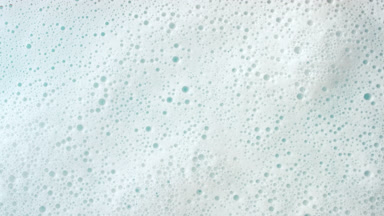 Macro shot of water with a lot of foam flows on cyan background