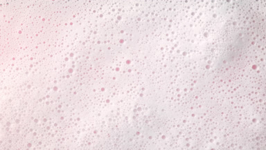 Macro of water with a lot of foam flows on pale pink background