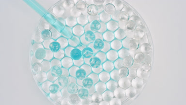 Cyan liquid drained from dropper in Petri dish with grey balls