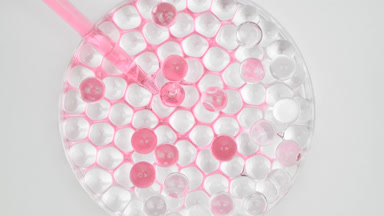 Pink oil drained in Petri dish with grey octagons sinking in it