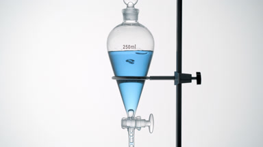 Pale blue transparent liquid drips from funnel, bubbles rise