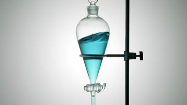 Cyan liquid waves inside glass vessel on grey ramp background