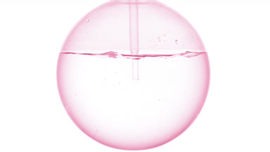 Clear liquid dropper into round flask, swirls, bubbles, white bg