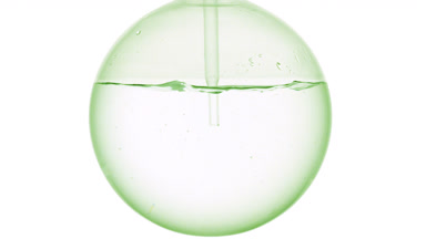 Clear liquid dropper into round flask, swirls, bubbles, white bg