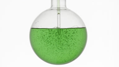 Green liquid swirls in round flask with dropper on white