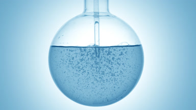 Pale blue liquid swirls in round flask with dropper on blue