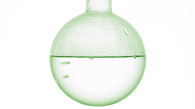 Clear liquid gently boils in round flask on white background