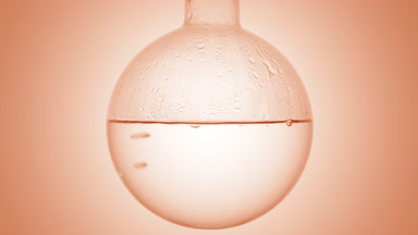Clear liquid gently boils in round flask on beige background