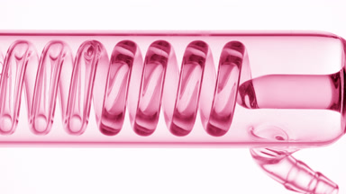 Pink liquid fills horizontal coil condenser on white background