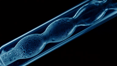 Blue liquid condensing on bulb lab condenser, black background
