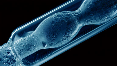 Blue liquid condensing on bulb lab condenser, black background