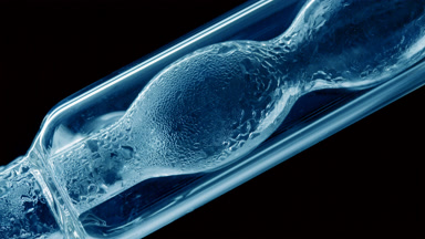 Blue liquid condensing on bulb lab condenser, black background
