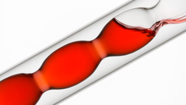 Red liquid pouring into inclined bulb condenser on white