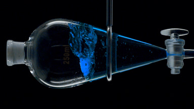 Blue liquid injection creates splashes inside on black backdrop
