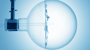 Clear liquid dropper into round flask, swirls & bubbles, blue bg
