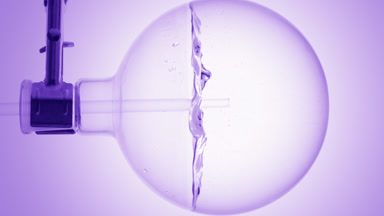 Clear liquid dropper into round flask swirls, bubbles, purple bg