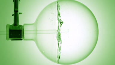 Clear liquid dropper into round flask, swirls, bubbles, green bg