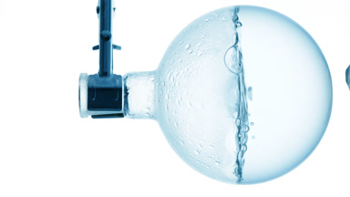 Pale blue liquid boiling in flask, condensation on white bg