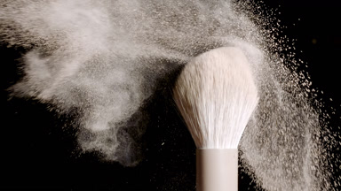 Close-Up of White Brush Flicking Beige Powder on Black
