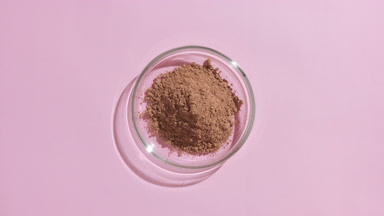 Overhead View of Brown Powder in Glass Dish on Pink Surface