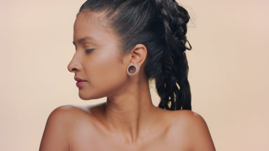 Hispanic woman with tan matte skin smiles to camera beige bg