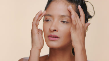 Hispanic woman moisturized honey skin strokes forehead beige bg