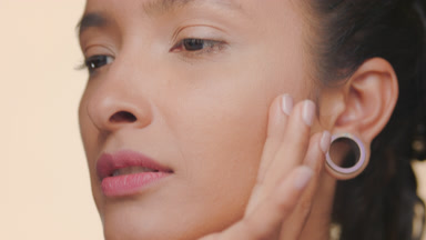 Latin woman nourished tan skin strokes forehead and cheek tan bg