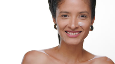 Hispanic woman with smooth skin applies cream on cheek
