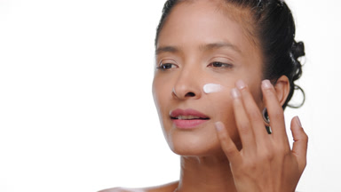 Argentinian woman applies cream on cheek tan skin on white