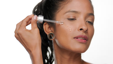 Latin american woman with honey skin applying serum on face
