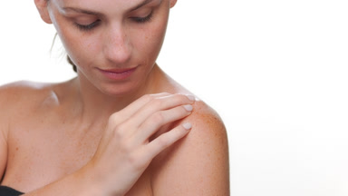 Hispanic woman with fair skin freckles strokes shoulder on white