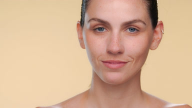 Fair-skinned spanish woman with freckles turns face on tan bg