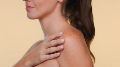 Young adult woman with freckles smiles shows moisturized skin