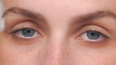 Latina with light complexion blue eyes looks at camera on tan bg