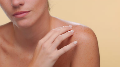 Woman with freckles strokes shoulder balanced skin on beige
